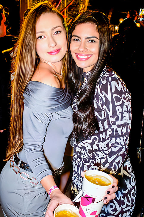 Duas mulheres, uma mulher de cabelos loiros longos, uma mulher de cabelos pretos longos sorrindo