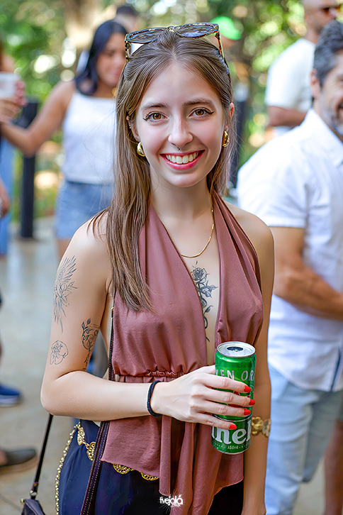 Uma mulher, cabelos lisos loiros longos com ocúlos no cabelo sorrindo 