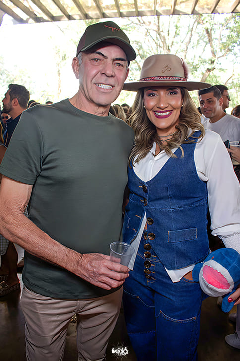 Duas pessoas, um senhor com boné sorindo e uma mulher com chapéu e caabelos loiros encaracolados sorrindo